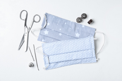 Homemade protective masks and sewing accessories on white background, flat lay
