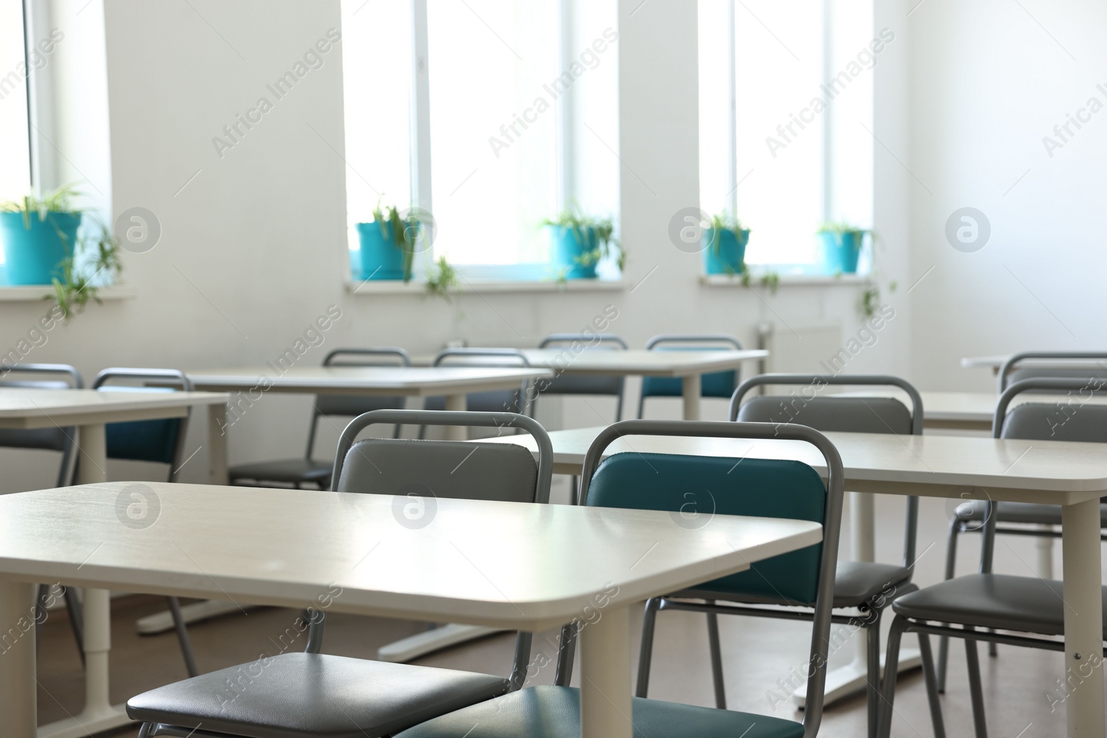 Photo of Empty school classroom with desks, windows and chairs