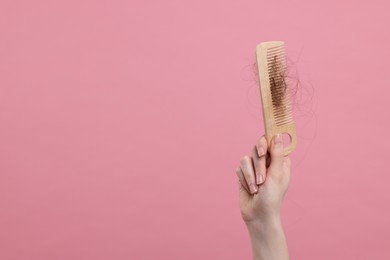 Woman holding comb with lost hair on pink background, closeup and space for text. Alopecia problem