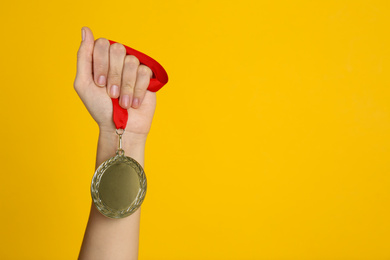 Photo of Woman holding golden medal on yellow background, closeup. Space for design