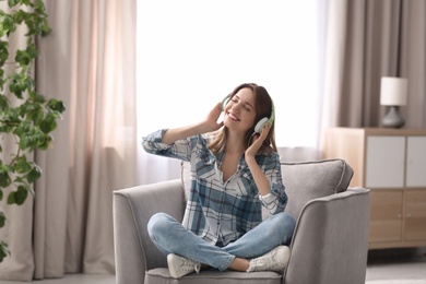 Photo of Young woman with headphones resting in armchair at home