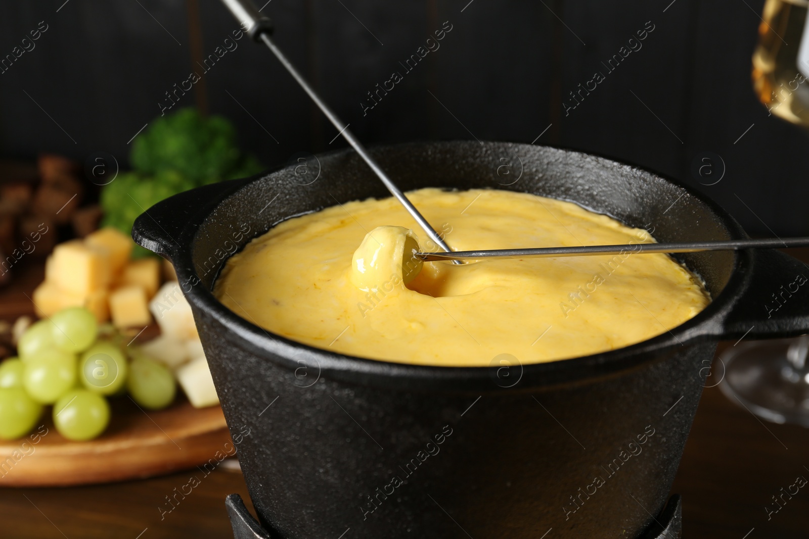 Photo of Dipping different products into fondue pot with melted cheese on table, closeup