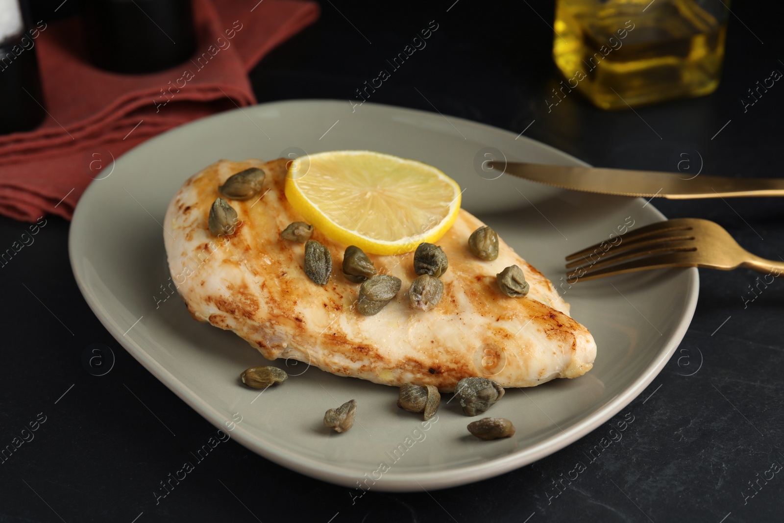 Photo of Delicious chicken fillet with capers and lemon served on black table, closeup