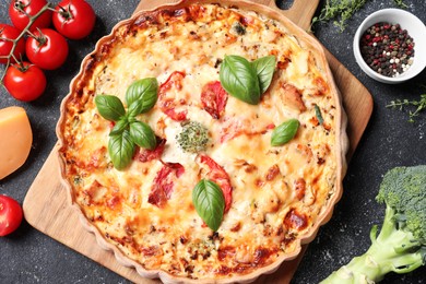 Photo of Tasty quiche with tomatoes, basil and cheese served on dark textured table, flat lay