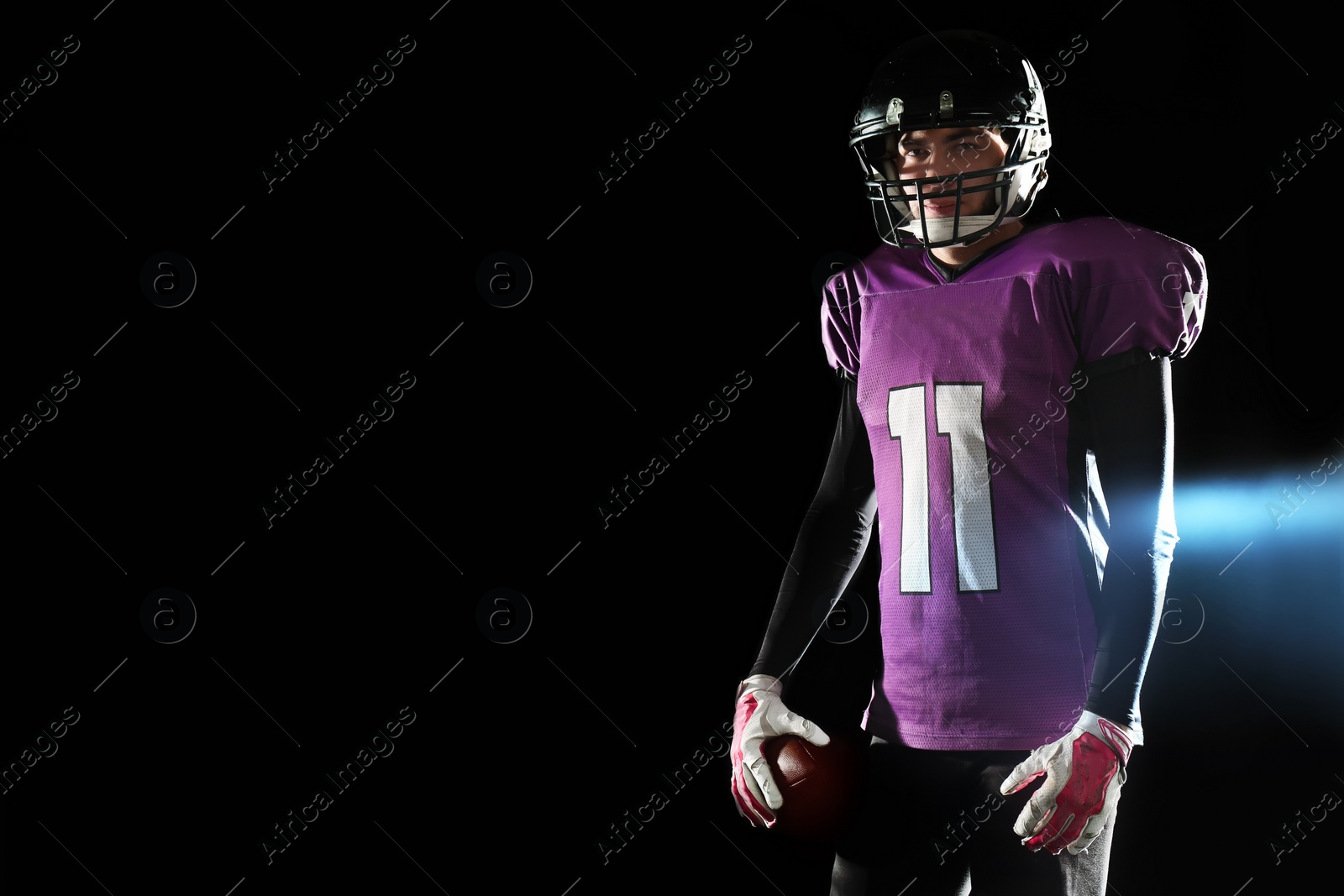 Photo of American football player with ball on dark background. Space for text