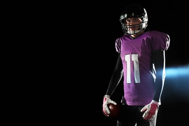 American football player with ball on dark background. Space for text