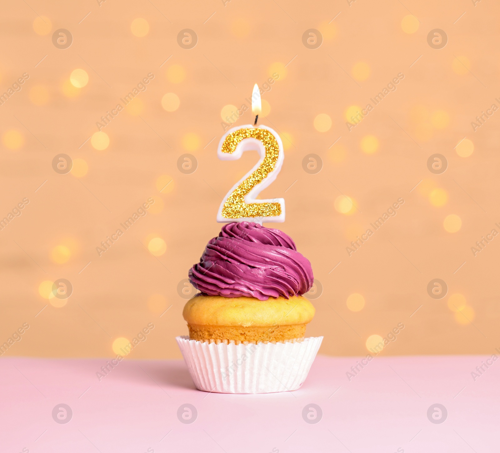 Photo of Birthday cupcake with number two candle on table against festive lights