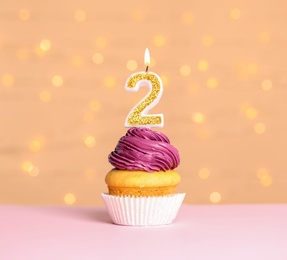 Photo of Birthday cupcake with number two candle on table against festive lights
