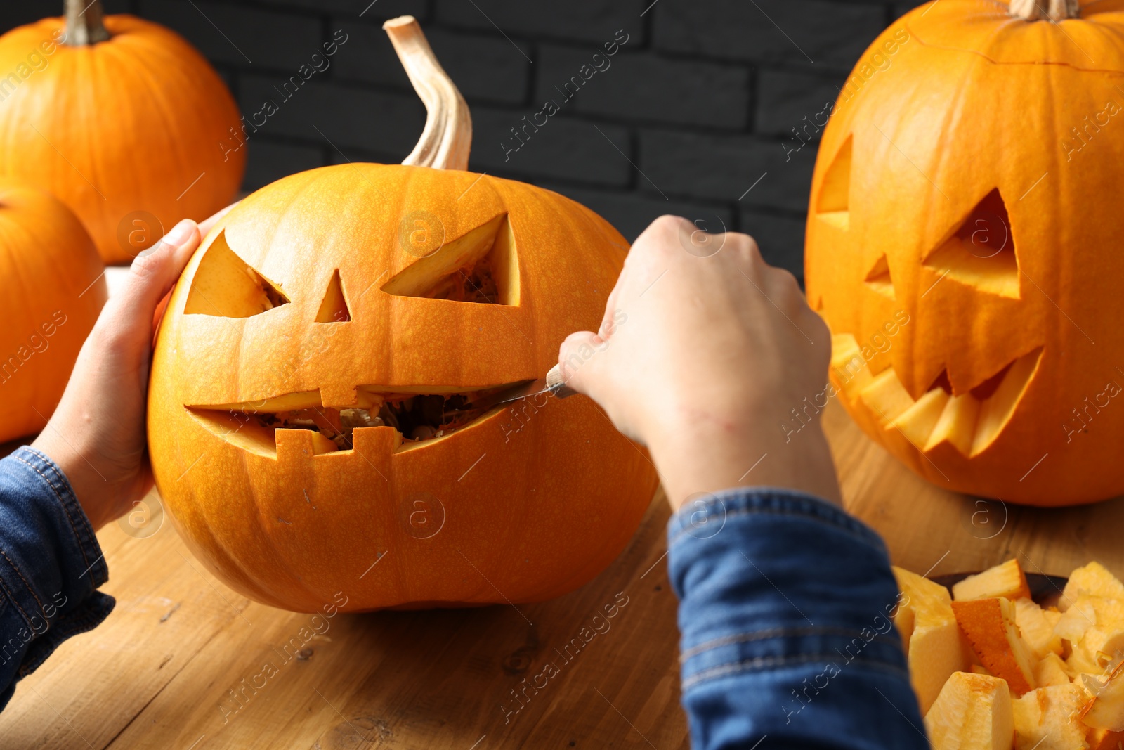 Photo of Woman carving pumpkin at wooden table, closeup. Halloween celebration