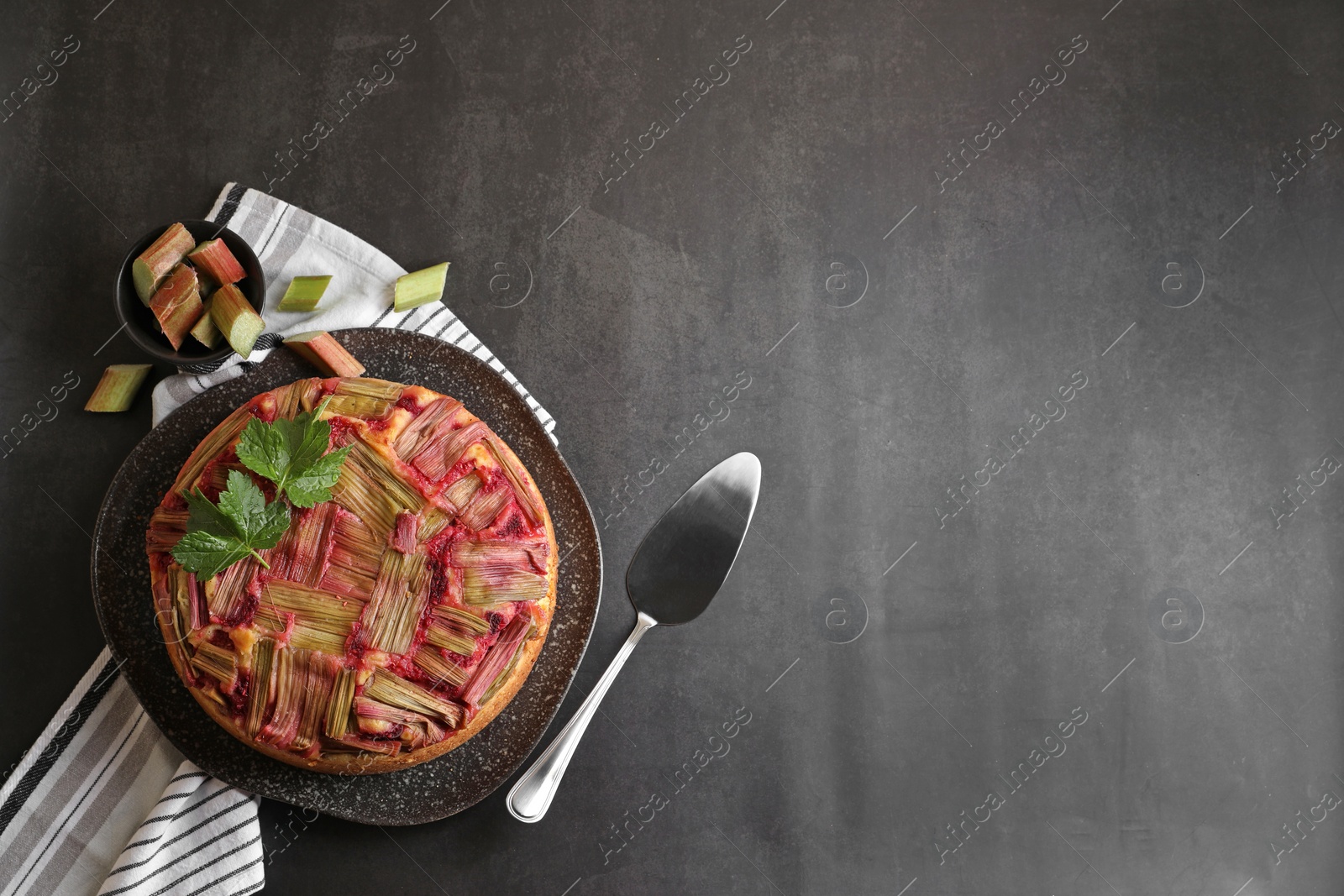 Photo of Freshly baked rhubarb pie, cut stalks and cake server on black table, flat lay. Space for text