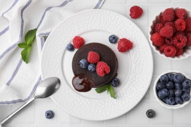 Photo of Plate with delicious chocolate fondant, berries and mint on white tiled table, flat lay