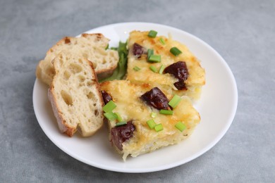 Photo of Tasty sausage casserole with green onion and bread on grey table, closeup