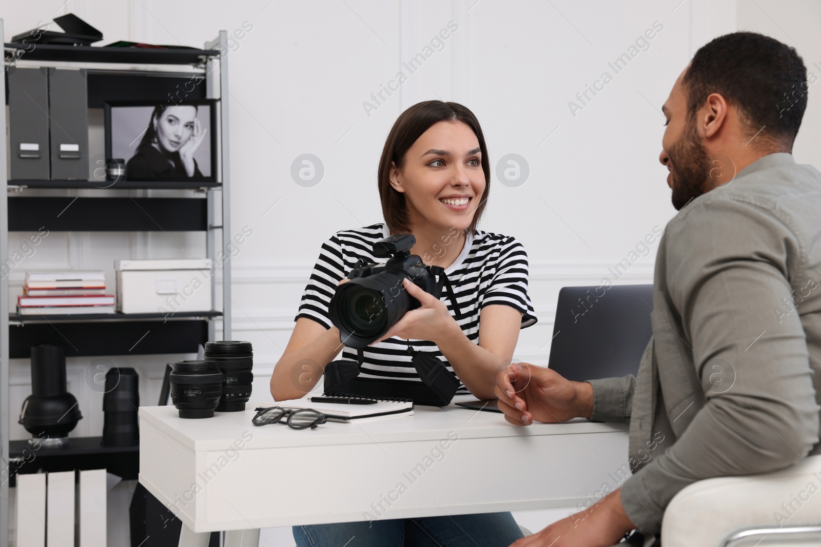 Photo of Young professional photographer showing camera to man in modern photo studio