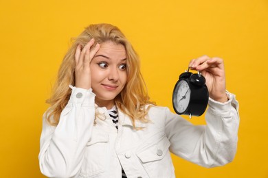 Photo of Emotional woman with alarm clock in turmoil over being late on yellow background