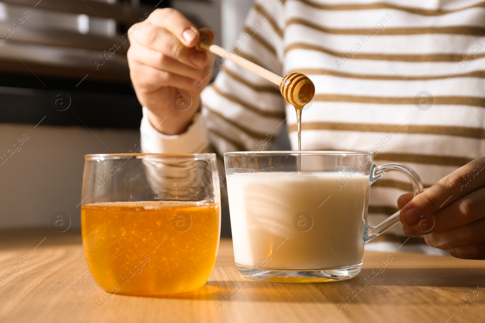 Photo of Woman adding honey to milk at wooden table closeup