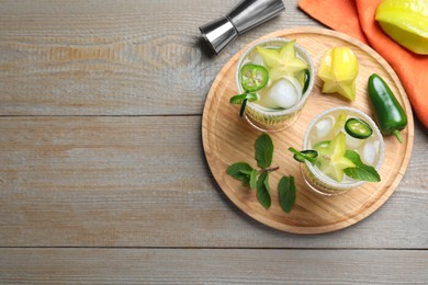 Glasses of spicy cocktail with jalapeno, carambola and mint on wooden table, flat lay. Space for text