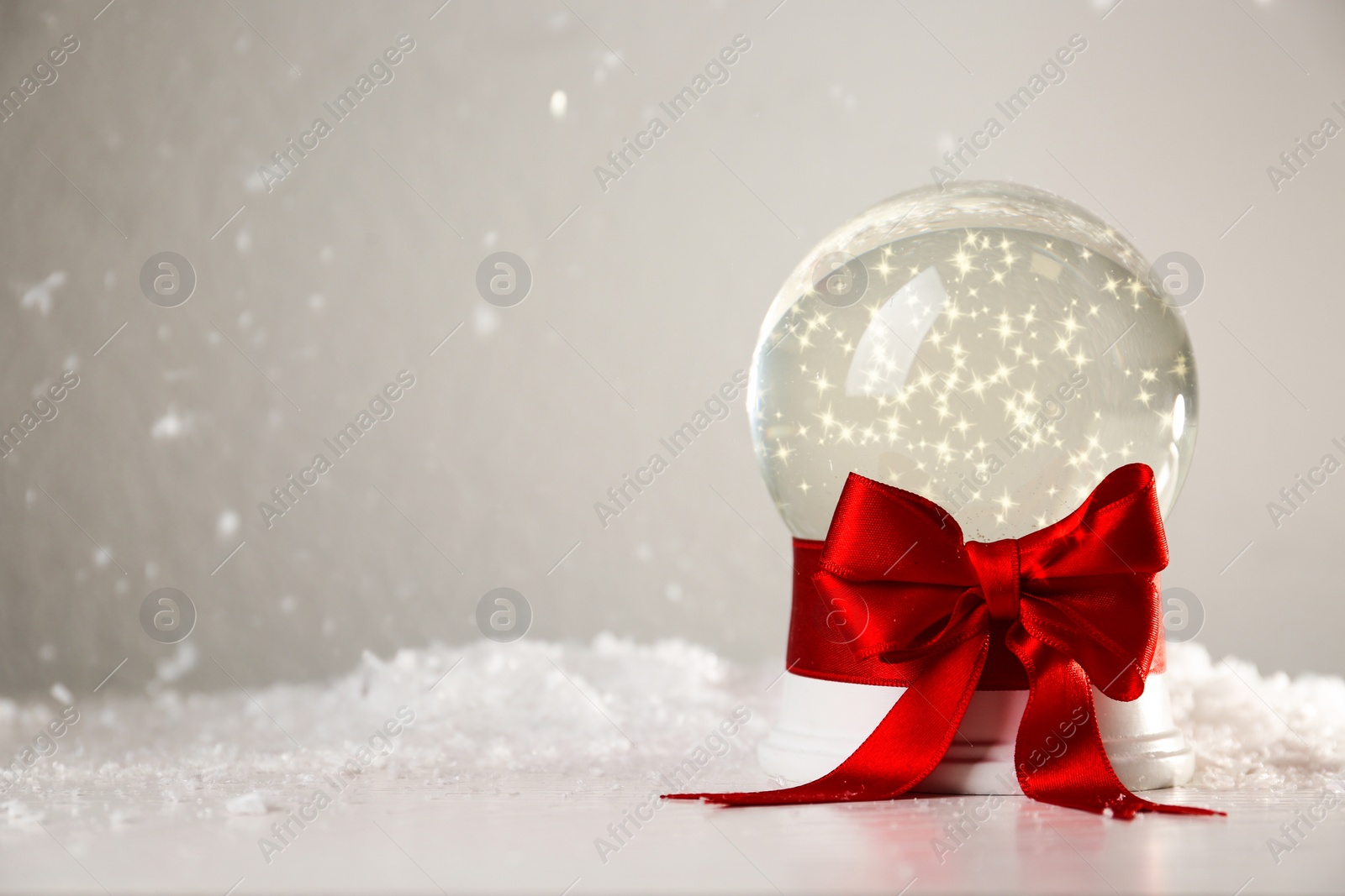 Photo of Beautiful Christmas snow globe with red bow on table against light background, space for text