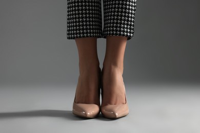 Businesswoman in beige shoes on grey background, closeup