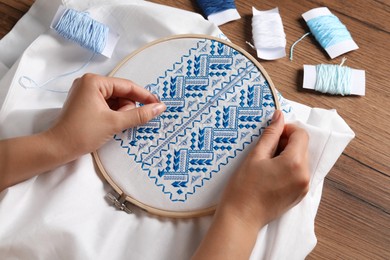 Photo of Woman embroidering white shirt with blue thread at wooden table, above view. Ukrainian national clothes