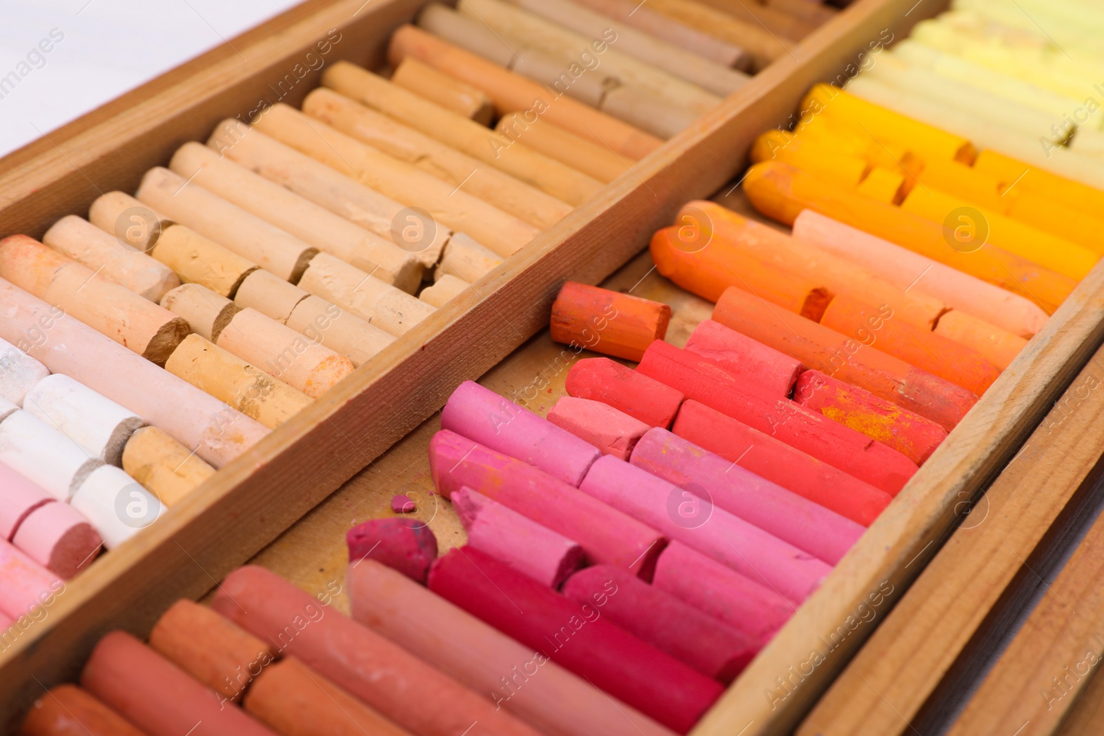 Photo of Set of soft pastels in wooden box as background, closeup. Drawing material