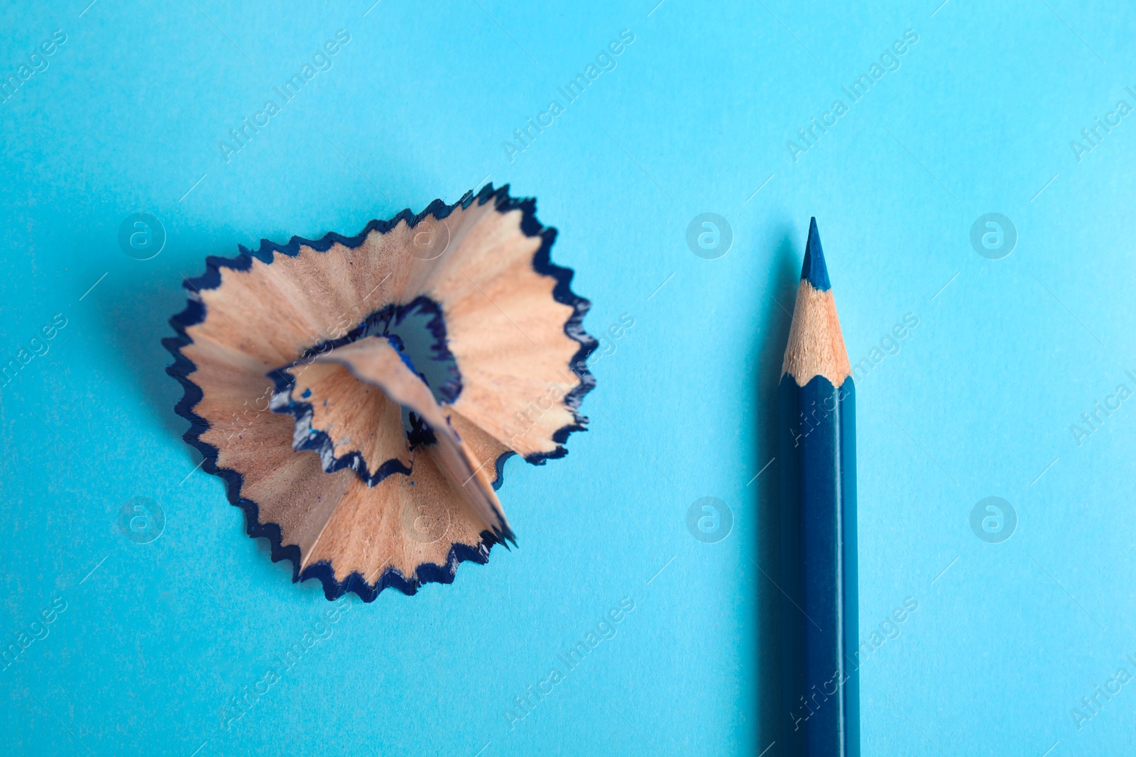 Photo of Color pencil and shaving on blue background, top view