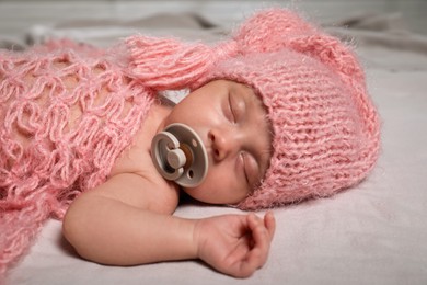 Photo of Cute newborn baby in warm hat sleeping on light bedsheet