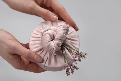 Furoshiki technique. Woman holding gift packed in fabric and beautiful pink flowers on gray background, closeup with space for text