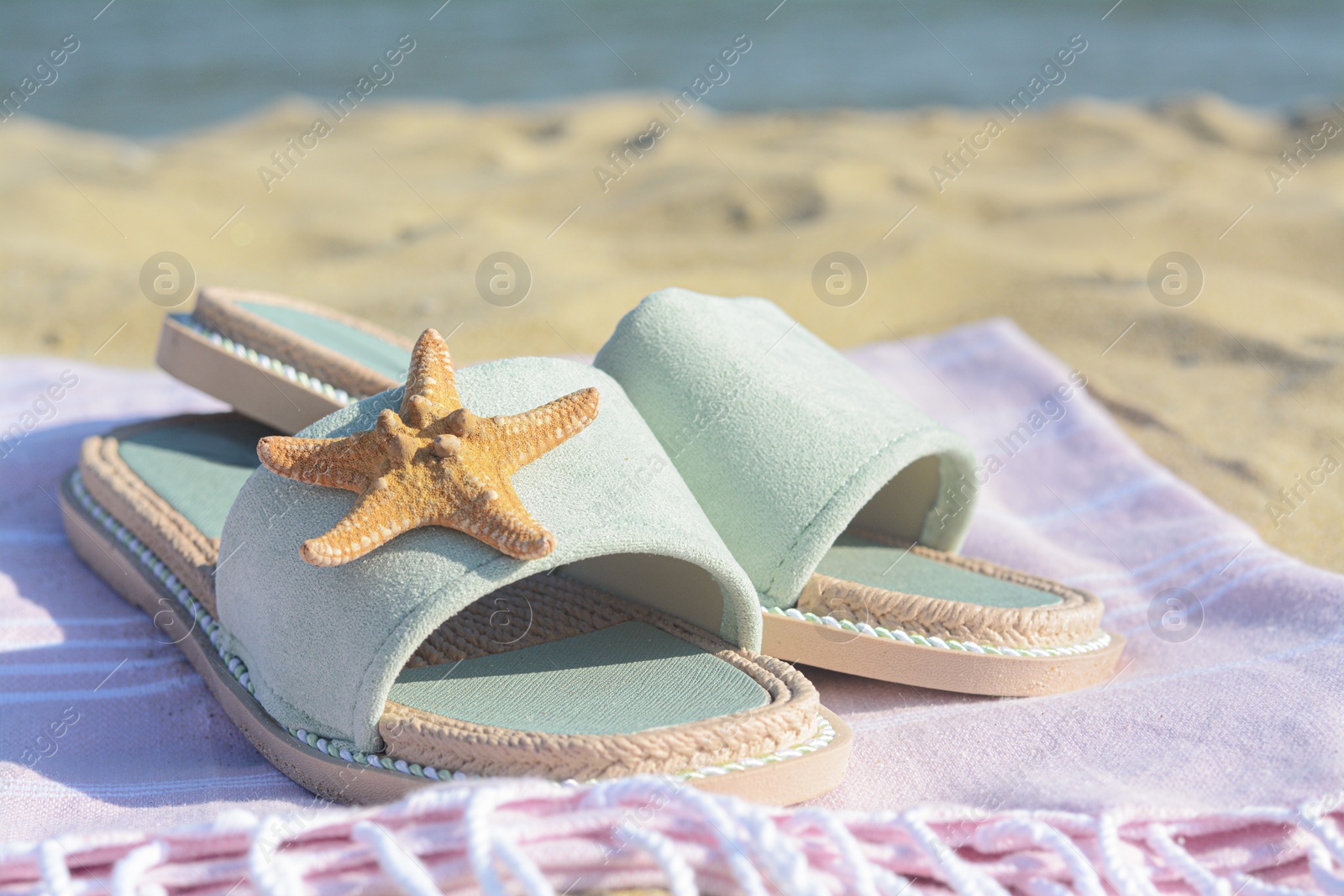 Photo of Pink blanket with stylish slippers and dry starfish on sandy beach near sea, closeup