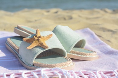 Pink blanket with stylish slippers and dry starfish on sandy beach near sea, closeup