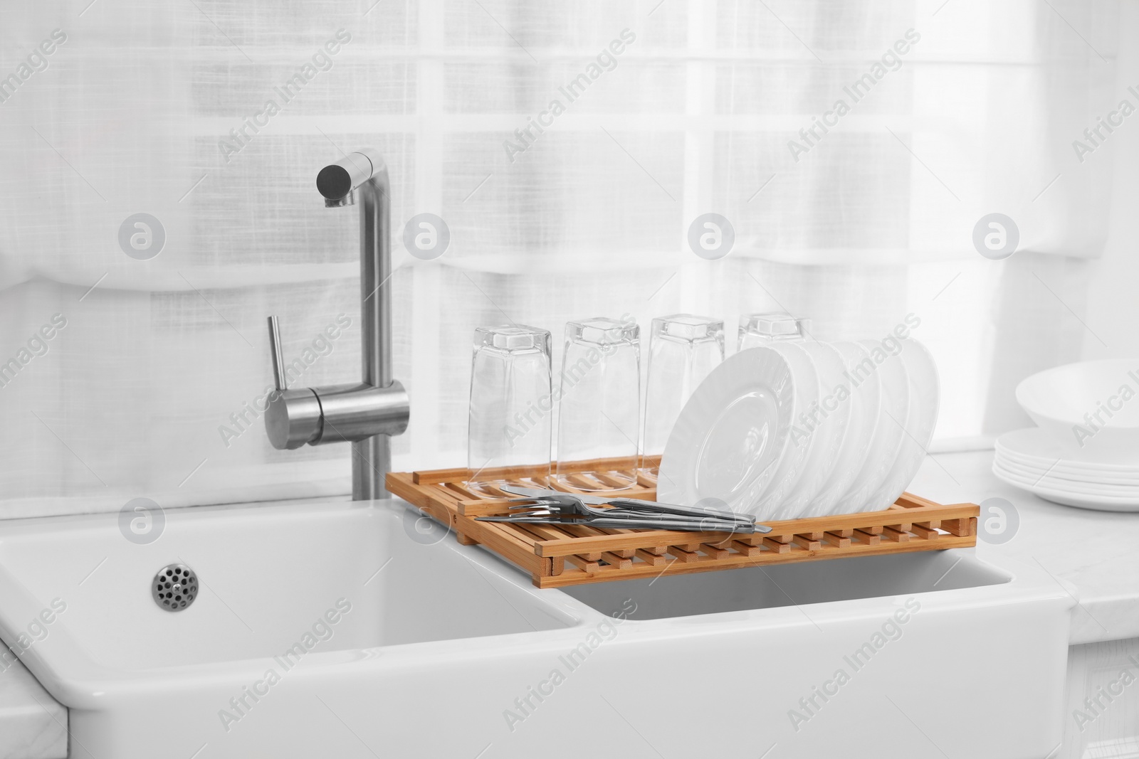 Photo of Sink and drying rack with clean dishes and cutlery on countertop in kitchen