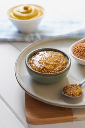 Photo of Bowl and spoon of whole grain mustard on white wooden table