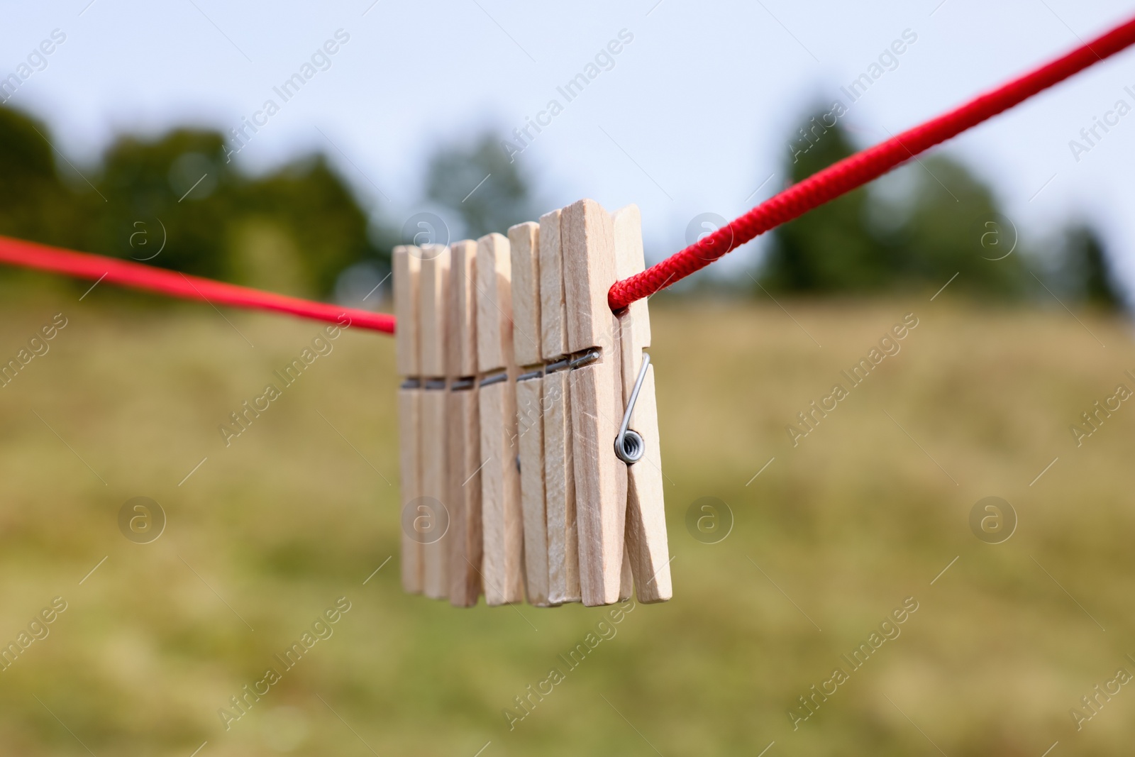 Photo of Wooden clothespins hanging on washing line outdoors, closeup