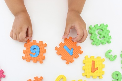 Little girl playing with colorful puzzles at white table, top view. Educational toy