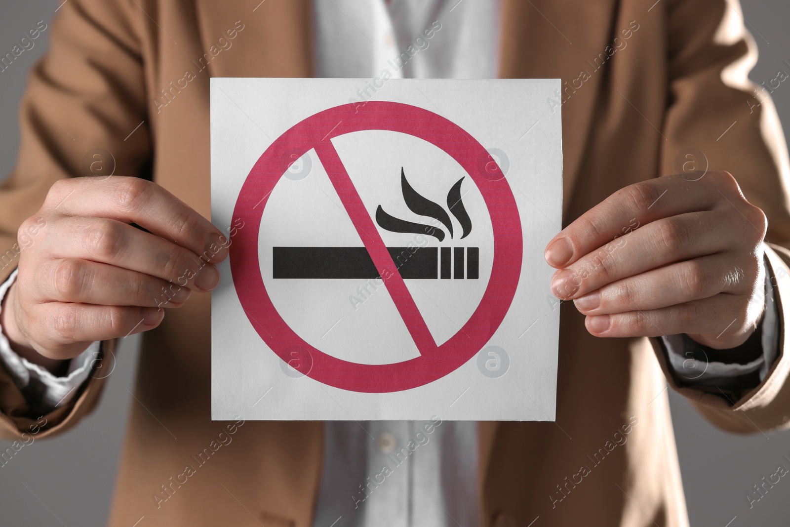 Photo of Woman holding card with no smoking sign on gray background, closeup