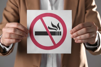 Woman holding card with no smoking sign on gray background, closeup