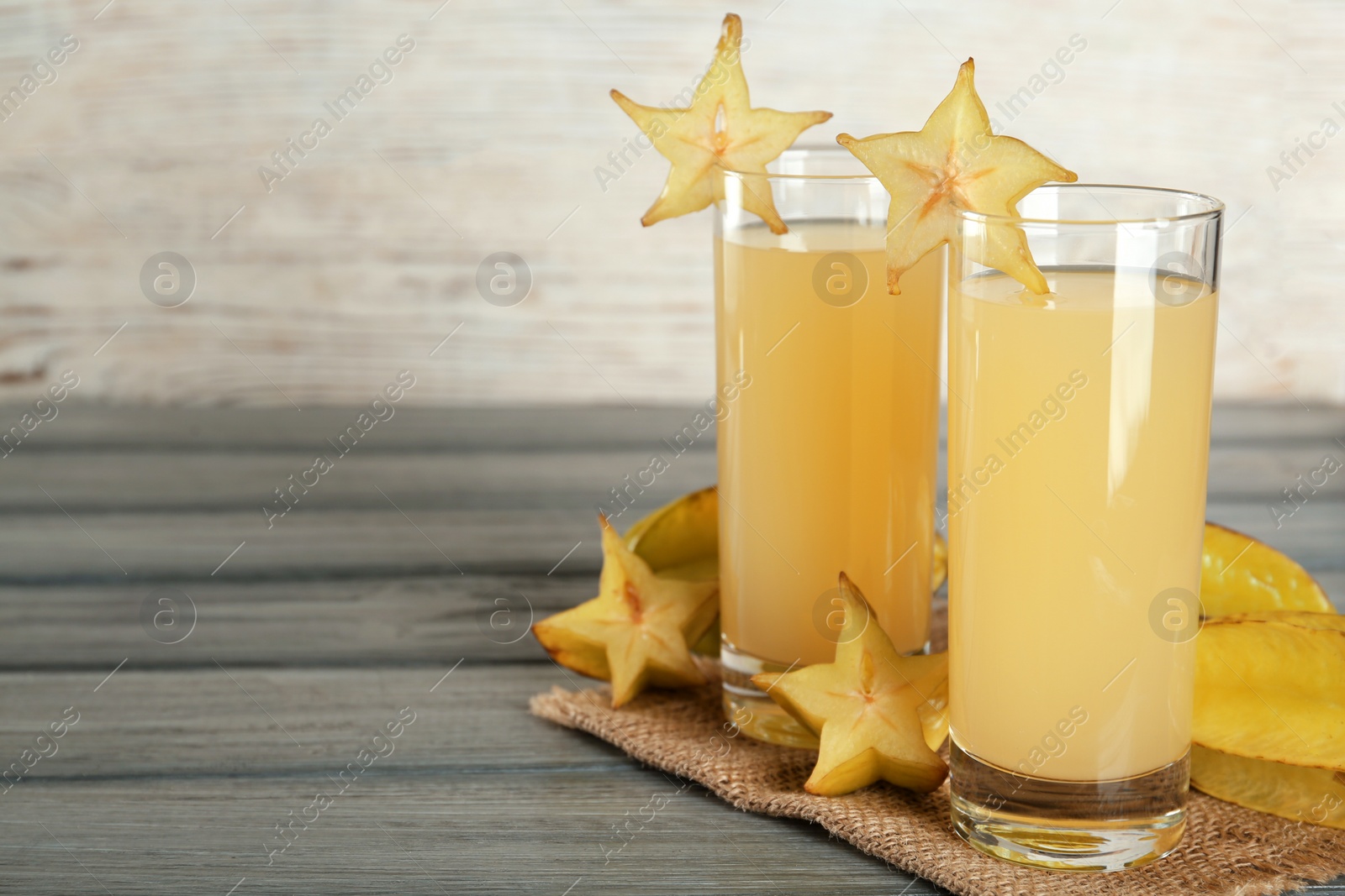 Photo of Delicious carambola juice and fresh fruits on grey wooden table. Space for text