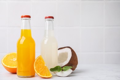 Photo of Delicious kombucha in glass bottles, orange, coconut and mint on white marble table, space for text