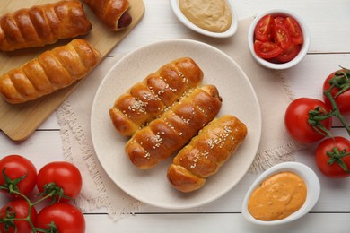 Photo of Delicious sausage rolls and ingredients on white wooden table, flat lay