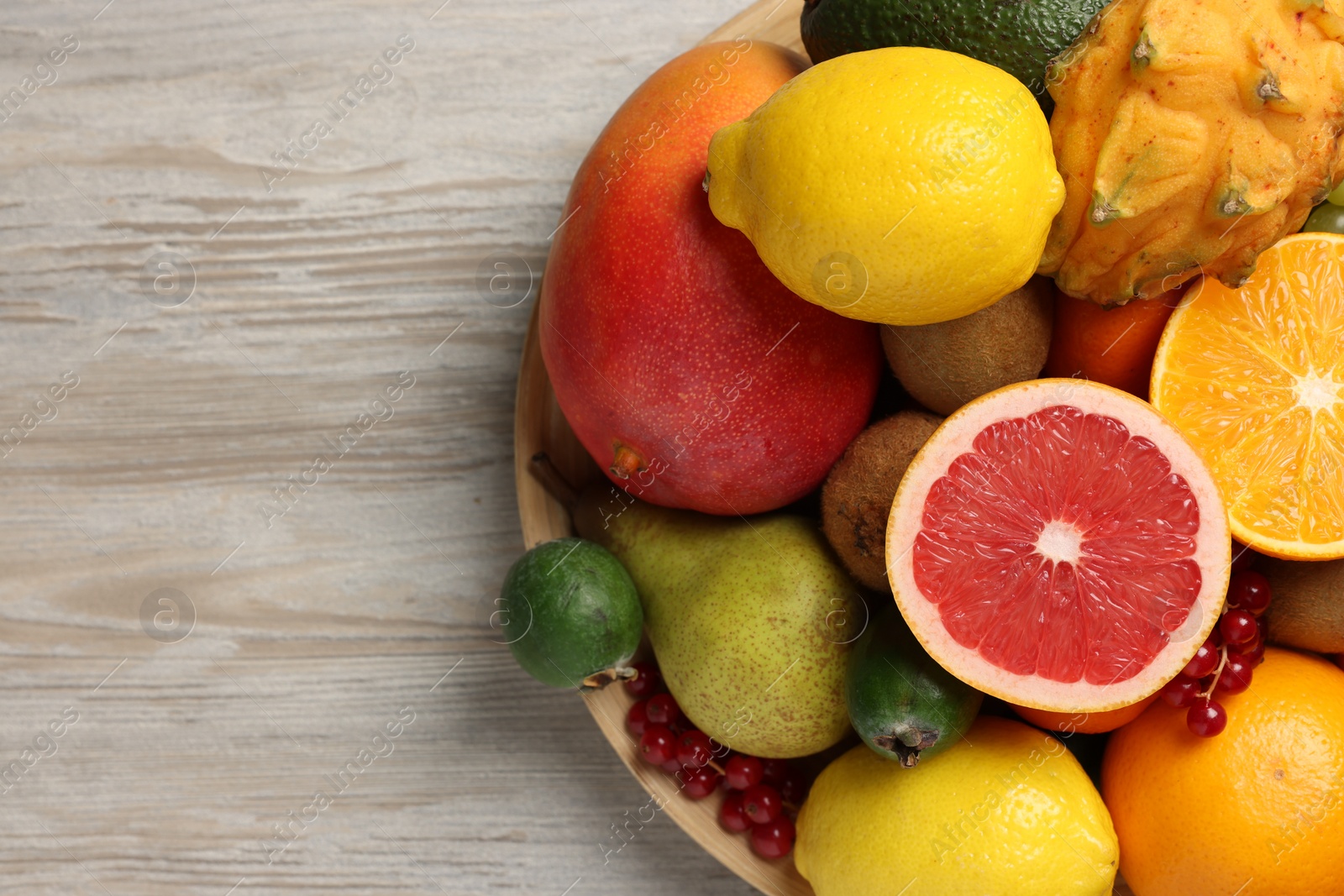 Photo of Different ripe fruits and berries on light wooden table, top view. Space for text