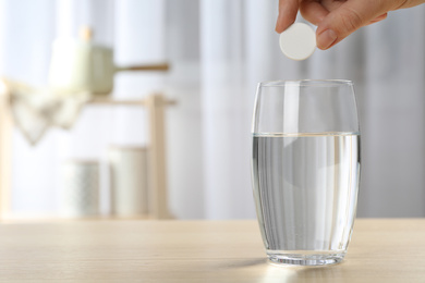 Woman putting tablet into glass of water indoors, space for text