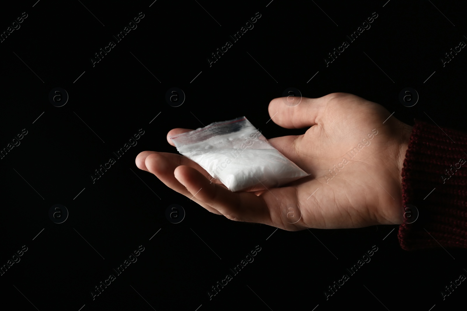 Photo of Drug dealer holding bag with cocaine on black background, closeup