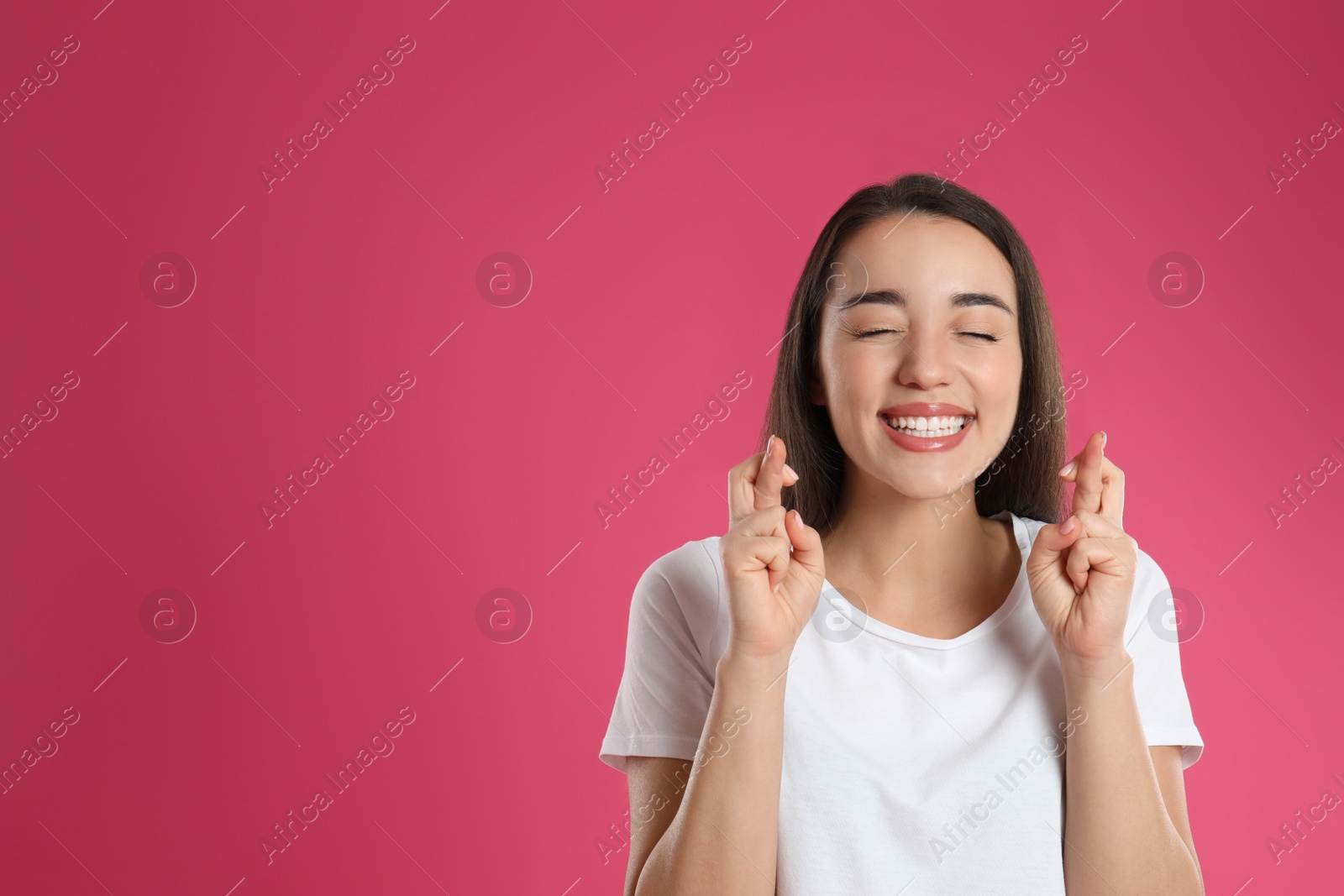 Photo of Woman with crossed fingers on pink background, space for text. Superstition concept