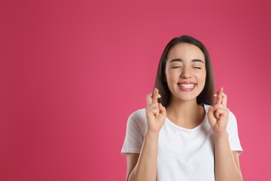 Photo of Woman with crossed fingers on pink background, space for text. Superstition concept