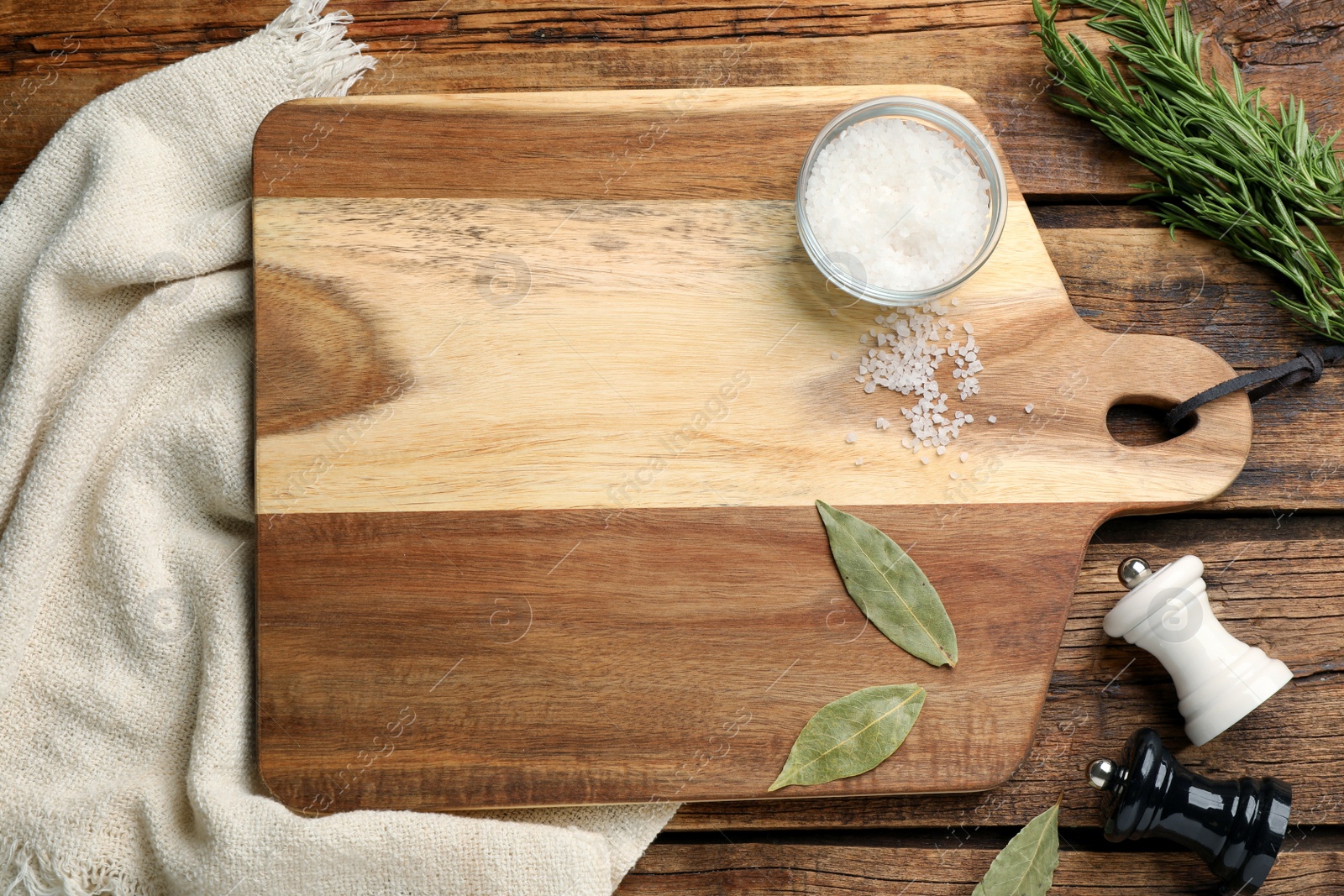 Photo of Cutting board and condiments on wooden table, flat lay. Cooking utensil