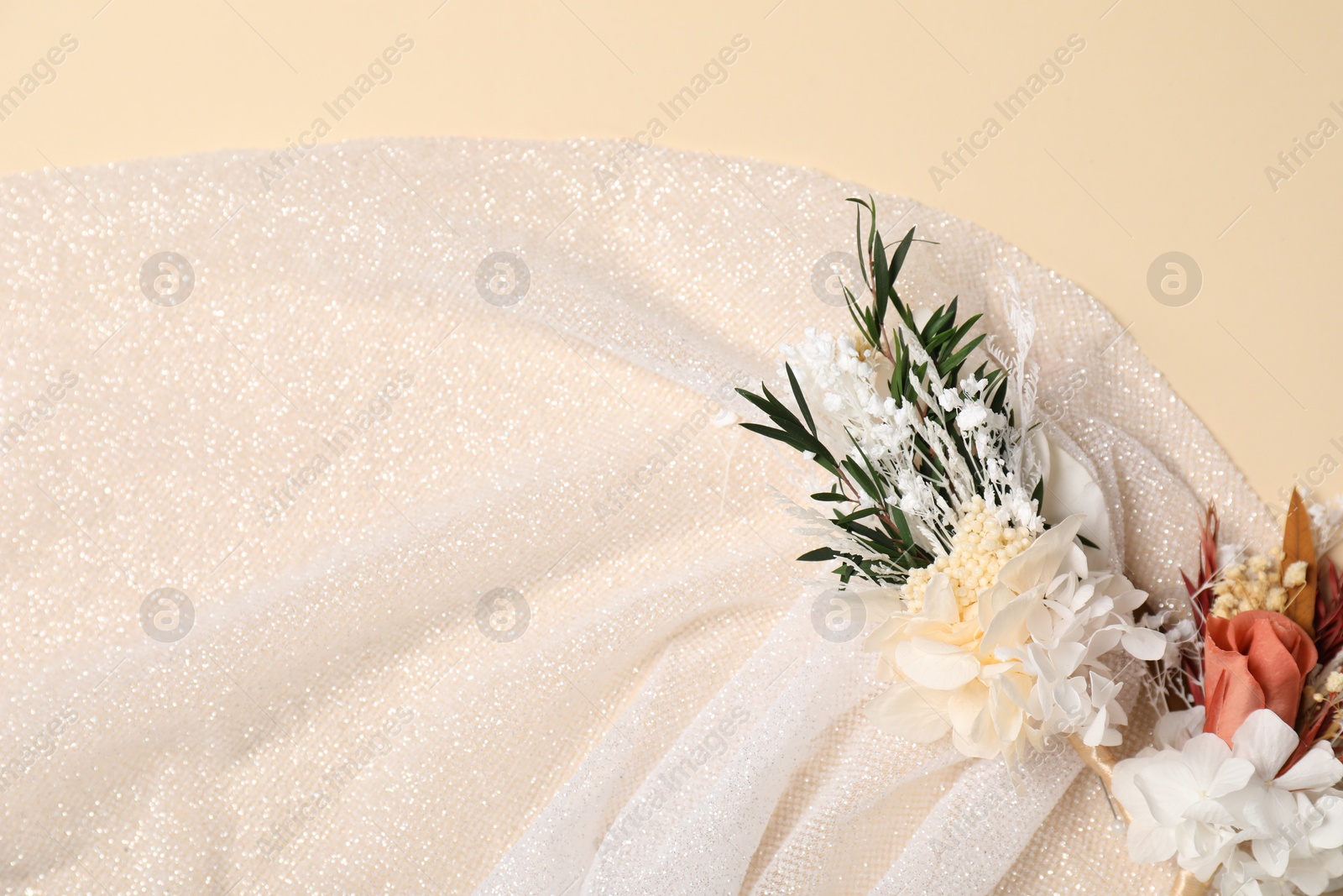 Photo of Stylish boutonnieres and white fabric on beige background, top view. Space for text