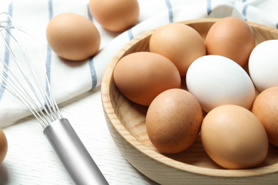 Photo of Chicken eggs and whisk on white wooden table, closeup