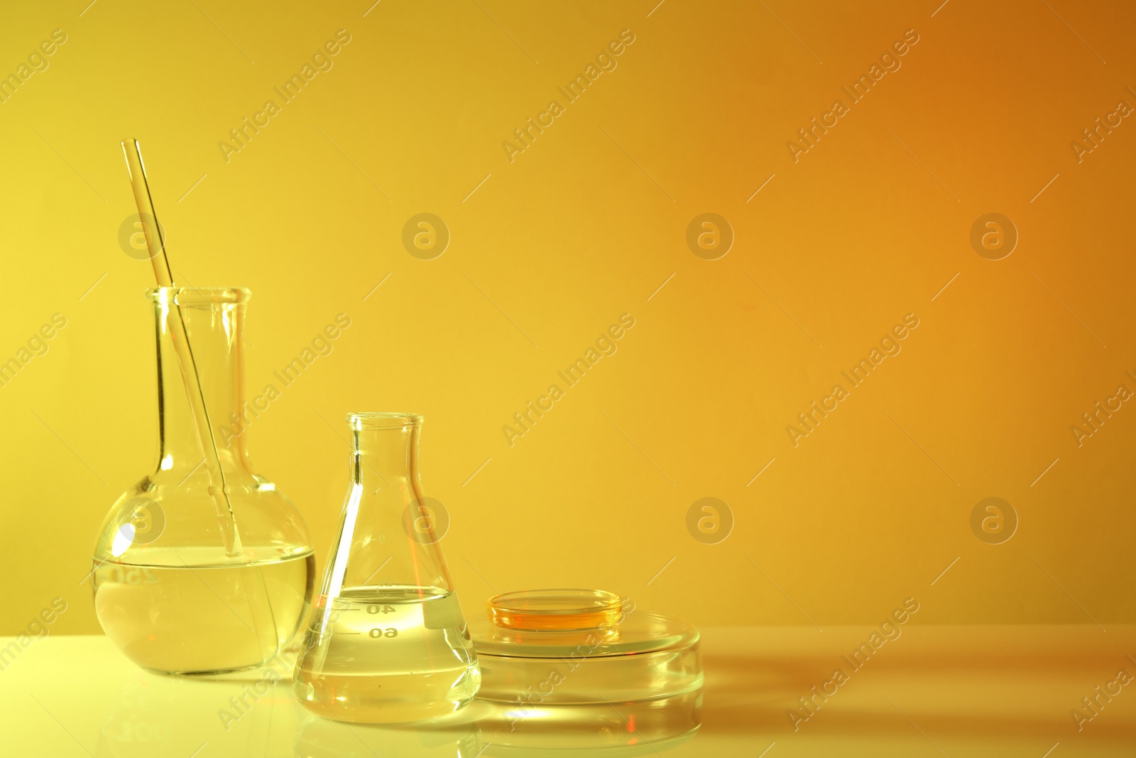 Photo of Laboratory analysis. Different glassware on table against yellow background, space for text