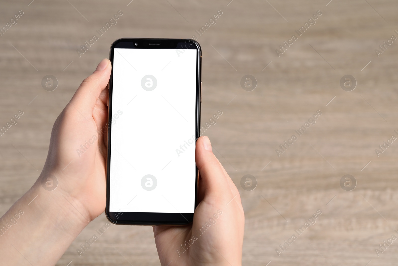 Photo of Woman holding smartphone with blank screen at wooden table, top view. Mockup for design