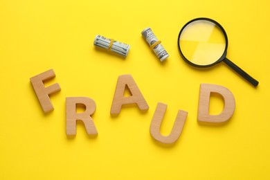 Photo of Word Fraud made of wooden letters, money and magnifying glass on yellow background, flat lay