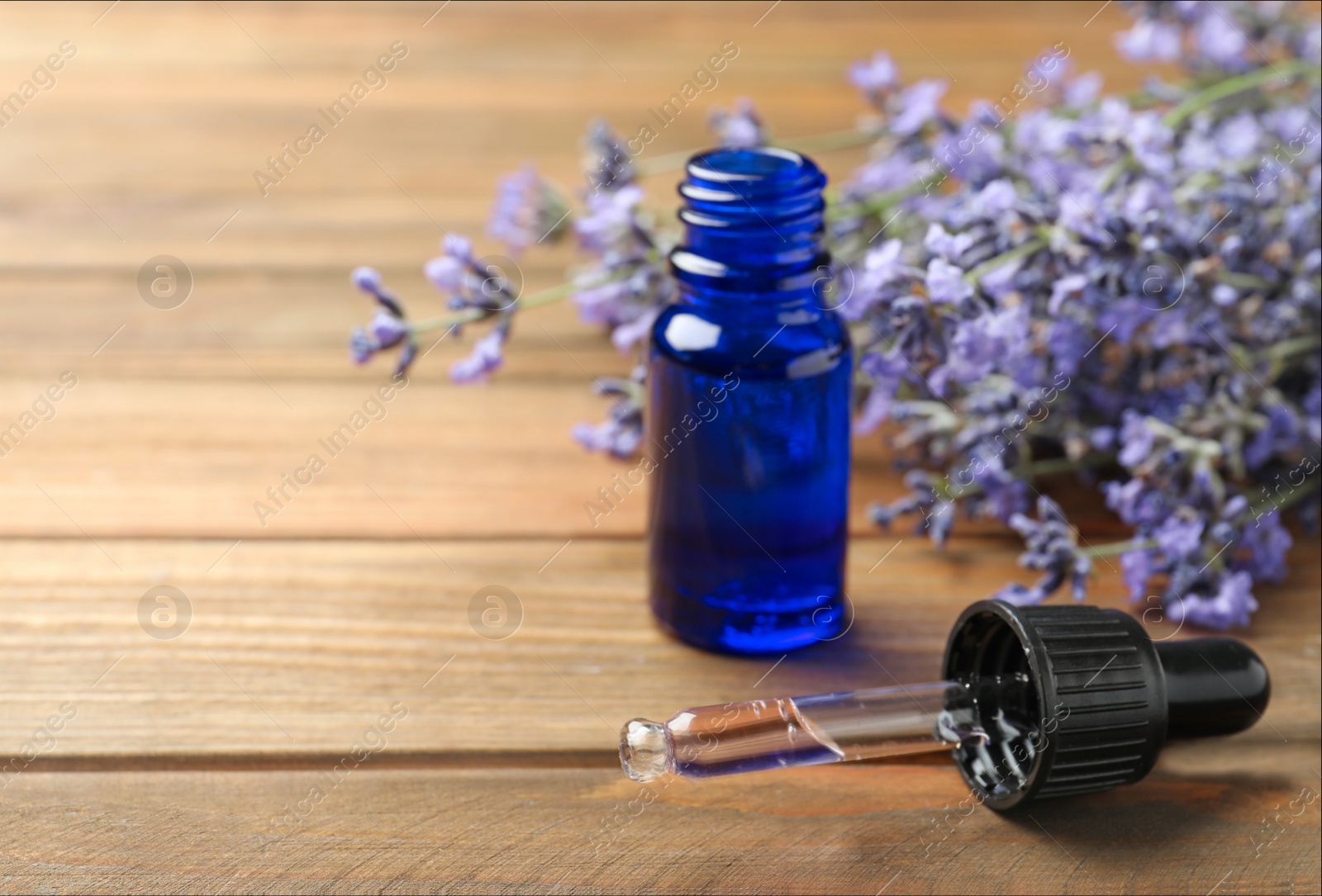 Photo of Bottle of essential oil and lavender flowers on wooden background. Space for text